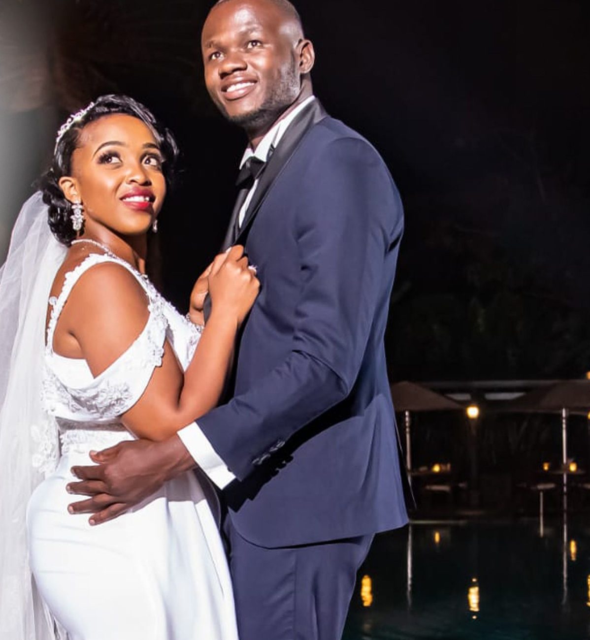 Bride and groom smiling together beside a lit pool at their evening reception